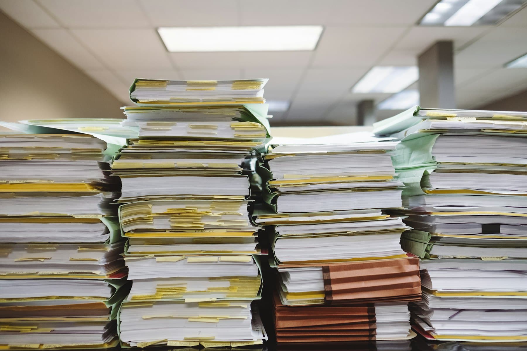 Stacks of loose paper documents and file folders piled on a desk