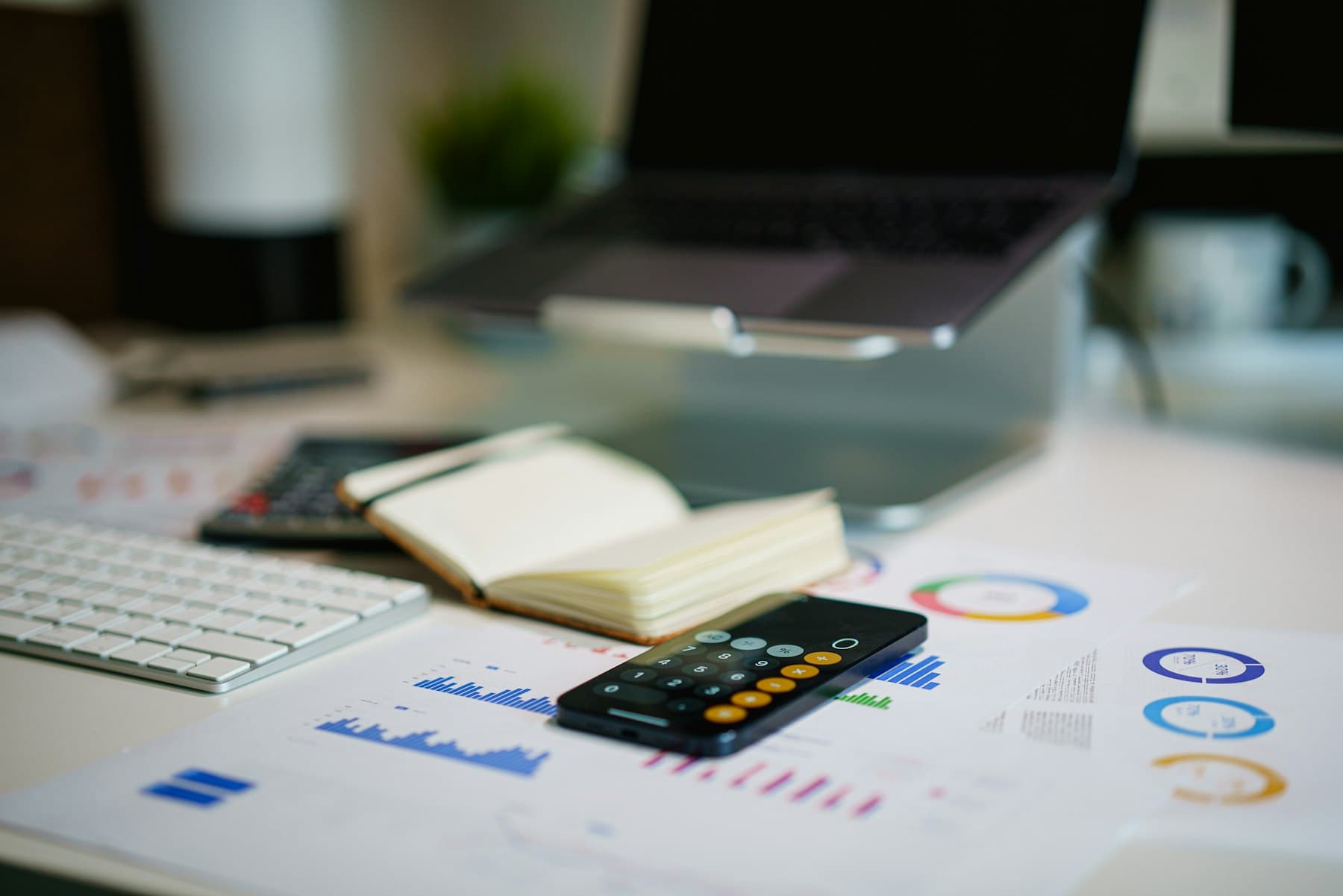 A desk with printed financial charts laid out beside a laptop